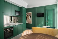 a kitchen with green walls and cabinets in the center, along with a dining room table