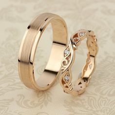 two gold wedding rings with diamond accents on a floral background, one is slightly bent to the side