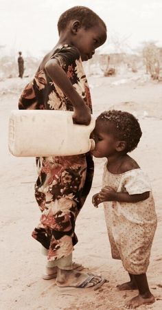 two young children are standing in the sand and one is holding a bottle over his head