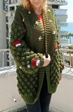 a woman wearing a green knitted cardigan with red and white pom poms