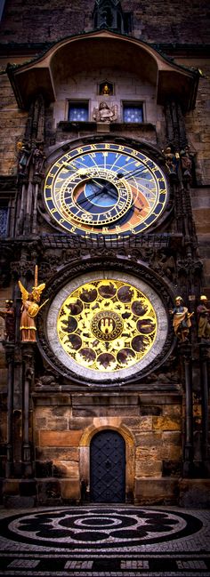 two clocks on the side of a building with an intricate design in front of it