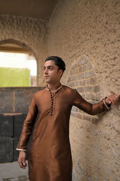 A brown silk kurta and fitted plain cotton silk pajama with gold embroidery on collar and sleeves and a matching motif on the arms, with round buttons to compliment the traditional look. Model wears a size Small. Long Sleeve Raw Silk Kurta For Transitional Season, Transitional Long Sleeve Raw Silk Kurta, Long Sleeve Cotton Silk Kurta For Traditional Ceremonies, Silk Dabka Kurta With Long Sleeves, Silk Long Sleeve Kurta With Dabka Detailing, Gold Cotton Silk Long Sleeve Kurta, Silk Long Sleeve Kurta With Dabka, Gold Long Sleeve Cotton Silk Kurta, Long Sleeve Naqshi Traditional Wear In Raw Silk