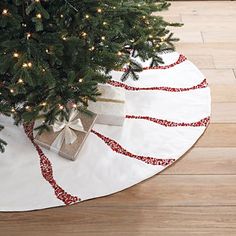 a christmas tree with presents under it on a white round tablecloth and wooden flooring