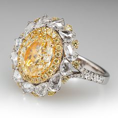 a fancy yellow and white diamond ring on a gray background with the center stone surrounded by smaller diamonds