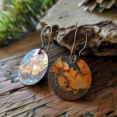 two earrings with rusted metal discs hanging from them on a wooden table next to a pine cone