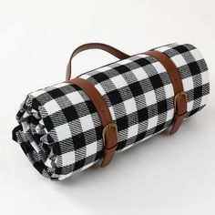 a black and white checkered duffel bag with brown straps on the bottom, sitting on a white surface