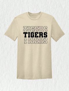 Introducing our Tigers Mascot Shirt, the perfect apparel for all the Tiger fans out there!  Whether you're a proud member of the Tigers team, a dedicated fan, or simply want to show your support, this shirt is a must-have addition to your collection. Designed with the iconic Tigers Mascot, this shirt captures the spirit and energy of your beloved team. Made with high-quality materials, this Tigers School Shirt is not only comfortable but durable as well. You'll love the softness of the fabric ag College Fan Apparel T-shirt With Team Name, Graphic Print Crew Neck T-shirt For Fans, Pre-shrunk Team-colored Fan Apparel T-shirt, Tri-blend T-shirt With Graphic Print For Fans, Team Spirit T-shirt With Screen Print For Fan Gear, School Spirit Short Sleeve T-shirt With Letter Print, Game Day Cotton T-shirt With Screen Print, Team-colored T-shirt With Screen Print For Fans, Football Season Fan Apparel T-shirt With Screen Print