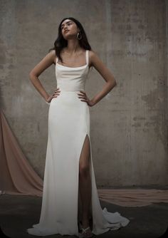 a woman standing in front of a wall wearing a white dress and high slit skirt