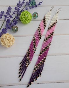 two pairs of beaded earrings sitting on top of a white table next to purple flowers