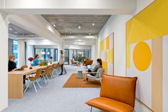 an office with people working on their laptops and sitting at desks in front of large windows