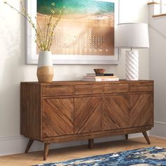 a living room with a large painting on the wall next to a dresser and lamp