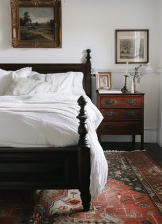 a bed with white sheets and pillows in a bedroom next to a painting on the wall