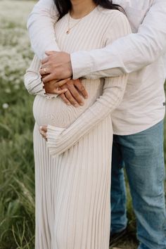 a man and woman standing next to each other in a field holding hands on their stomach