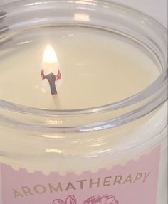 a candle that is inside of a glass jar with some writing on the label in front of it