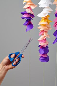 a person is holding scissors in front of some paper flowers that are hanging from strings