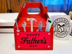 a red father's day box with tools in it sitting on a table next to a coffee mug