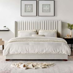 a white bed with two framed pictures on the wall above it and a rug in front of it