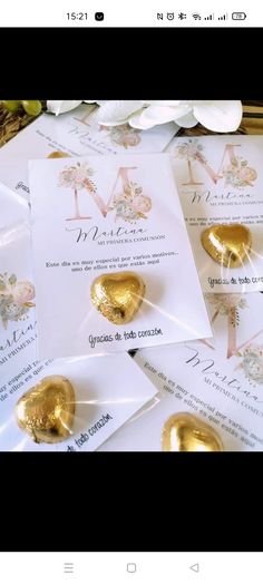 some gold foil hearts are on top of white envelopes and paper with the letter m