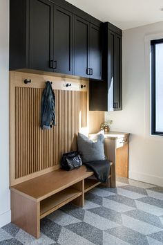 a wooden bench sitting under a window next to a coat rack and cabinets in a room