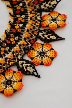 an orange and black beaded necklace on a white surface with beads in the shape of flowers