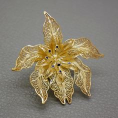 Introducing a stunning vintage orchid flower brooch by Topazio Portugal, a symbol of timeless elegance and charm. This meticulously crafted delicate filigree brooch is crafted of 800 silver, with a lustrous gold-plated coating. The intricate design is elevated by shimmering blue enamel stamens, capturing the beauty of the orchid. Hailing from the 1960's to 1970's era, this piece is not just jewelry but a true relic of the past. Whether it's for a special occasion or everyday elegance, this brooc Vintage Sterling Silver Jewelry, Orchid Flower, Silver Filigree, Flower Brooch, Vintage Sterling Silver, Vintage Gold, Orchids, Sterling Silver Jewelry, Portugal