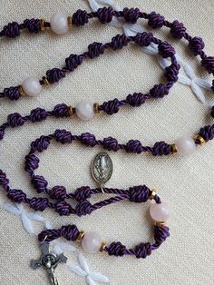 This rosary combines the strength of a knotted rosary with the beauty of a metal rosary. It is made with a deep purple nylon twine, gold-toned spacers, rose quartz beads, and a silver-toned miraculous medal and crucifix. Stainless steel double loop jump rings ensure the pendants won't come off.  The colors of the PREPARE rosary are significant. Purple and pink are the liturgical colors that are used during the seasons of Advent and Lent. Purple represent penance, preparation and sacrifice.  Knotted rosaries are the kind of rosaries you can do life with. They can be stuffed in a pocket or purse and hold up beautifully to daily use. Do you like to handle or turn the knots or beads while praying? These rosaries won't break. The addition of Our Father beads, a miraculous medal and a real cruci Handmade Adjustable Purple Rosary, Handmade Adjustable Rosary For First Communion, Knotted Rosary, Liturgical Colours, Personalized Rosary, Custom Rosary, Heart Knot, First Communion Gifts, Purple Jade