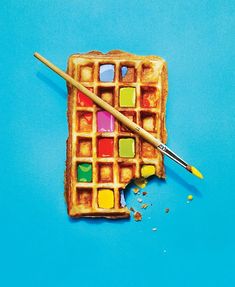 a waffle with colored squares and a paintbrush next to it on a blue background