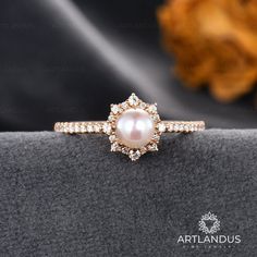 a pearl and diamond ring sitting on top of a black velvet cushion with an orange flower in the background