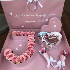 a pink heart shaped box filled with lots of candy and flowers sitting on top of a table