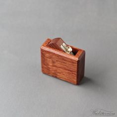 a wooden ring box with two rings in it on a gray surface and the lid is open