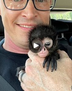 a man is holding a baby spider in his arms and smiling at the camera while sitting in a car