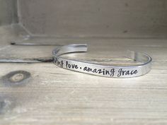 From the beloved Amazing Grace hymn Unending Love. Amazing Grace. is hand stamped on an aluminum bracelet. This bracelet measures 6” x 1/4” and can be formed to fit most wrist sizes. It looks great alone or layered with any of our other bracelets.  ~Metals Available~  Aluminum - We use 1100 Pure Food Safe Aluminum. This aluminum will not tarnish like sterling silver, or cause skin reactions like nickel, brass, or copper can. They are very lightweight and comfortable to wear. Aluminum is ... Grace Bible Verses, Amazing Grace Hymn, Scripture Bracelet, Verse Bracelet, Unending Love, Bible Verse Bracelet, Aluminum Bracelets, Christian Bracelets, Copper Metal