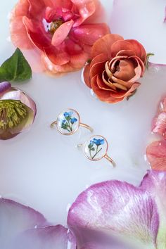 three rings with flowers on them sitting next to each other in front of some petals