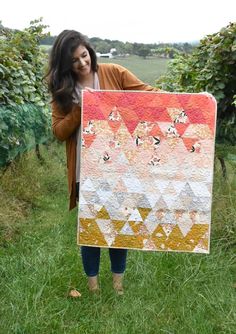 a woman holding up a quilt in the grass