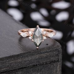 an engagement ring with a pear shaped green stone surrounded by small white diamonds on a wooden surface