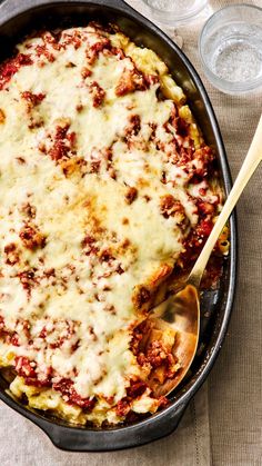 a casserole dish with meat and cheese in it on a table next to water glasses