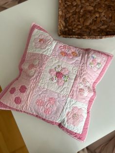 a pink pillow sitting on top of a white table next to a brown basket filled with nuts