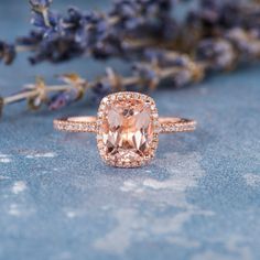 a pink diamond ring sitting on top of a blue surface next to lavenders and flowers