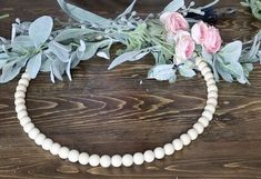 a white beaded necklace with pink flowers and greenery around it on a wooden surface