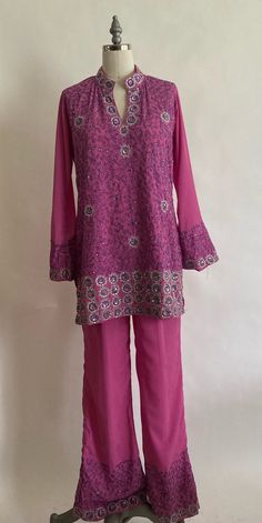 "1990's custom made fuchsia kurti set features a long tunic with a split hem at the sides, bell sleeves and split neck. Trousers are flared with a pleated high waist with elastic in the back . Top and pants are embellished with silver embroidery and sequins. Fabric is a lightweight polyester crepe and is lined with the same crepe within the bodice area. Pants are lined in a lightweight poly chiffon. Both top and bottom are in very good condition though the trousers have a small ink stain near on