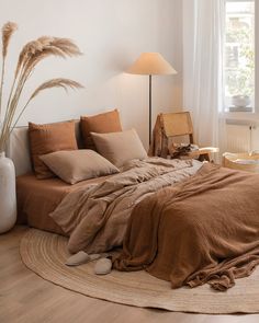 a bed with brown linens and pillows in a white room next to a window