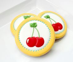 two cookies with cherries on them are sitting in a white box, one is yellow and the other is red