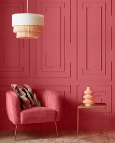 a living room with pink walls and a chair in front of a table that has a lamp on it