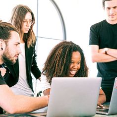 three people looking at a laptop screen while another looks on from the other side with their arms crossed