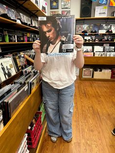 a person holding up a magazine in a store aisle with shelves full of cds and dvds