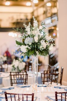 a tall vase filled with white flowers on top of a table covered in blue and white linens