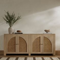 a sideboard with wicker doors and two vases on top of it next to a striped rug