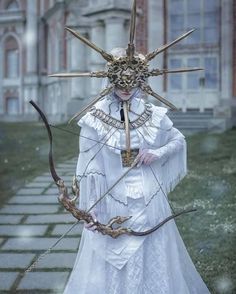 a woman dressed in white holding a bow and arrows with her head made out of sticks