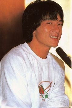 a man sitting in front of a microphone and smiling at the camera while wearing a white shirt