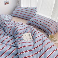 a bed covered in blue and red striped sheets with a cup on the pillow next to it